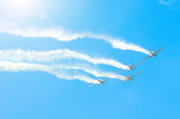 Light engine airplane with a trace of white smoke fly in groups in the blue sky with sunlight and glare