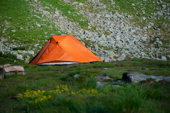 A bright orange tent on grass with beautiful rocky hill in background. No people around. Peace and quiet.  activeadventureautumnbackgroundbeautifulbeautybrightcampclimbconceptdaylightenvironmentequipm