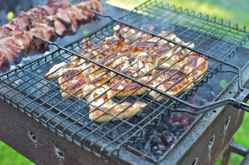 Closeup of chicken wings frying in a barbecue grill. Coal in the background. 