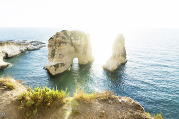 Naklejka premium Blue Sea and cliffs with grass around Pigeon rock with backlight sunlight, Beirut, Lebanon