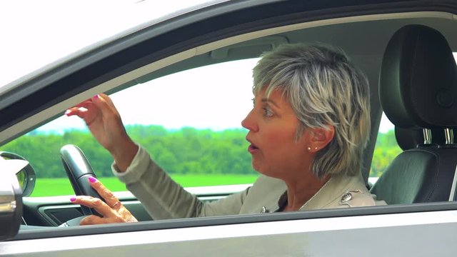 Middle aged woman sits in the car and complains on traffic situation - car stands on the verge of road in countryside 