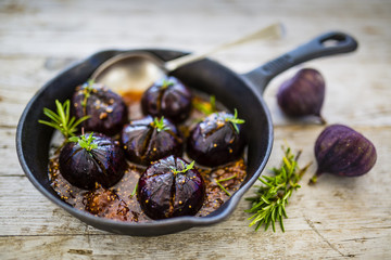 Oven-baked figs with herbs and honey on frying pan with spoon. Italian food.