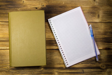 Old closed book, notepad and pen on wooden desk