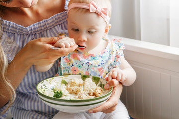 Closeup portrait of young woman mother feeding her girl daughter with vegetables broccoli cauliflower. Healthy organic food for children. Candid lifestyle family life. Baby trying finger food