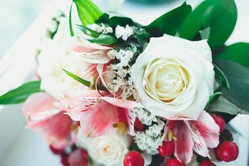 Gold wedding rings on a white table with a bouquet of brides from beautiful flowers
