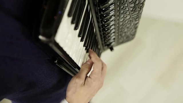 Close-up of a man's right hand playing on a black accordion.