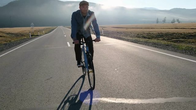 Young handsome man riding at vintage bicycle in the country road. Sporty guy cycling at the track. Male cyclist riding fixed gear bike at highway. Healthy active lifestyle 20s 4k.