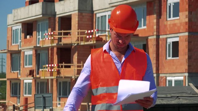 Construction worker studies some documents in front of building site