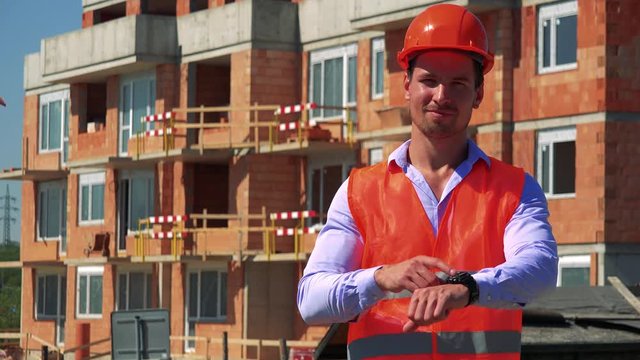 Construction worker points to his watch in front of building site