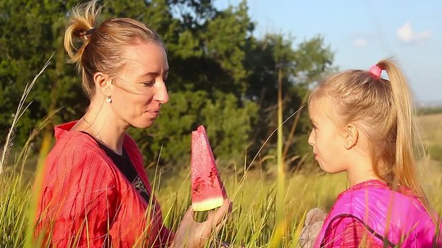 Two smiling girls eats slice of watermelon outdoors on the farm. Mother and daughter spend time together. Country style.