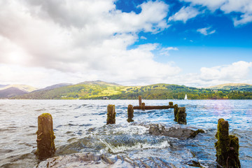 Windermere is the largest natural lake in England. Sunny cloudy sky. Remains of an old wooden pier.