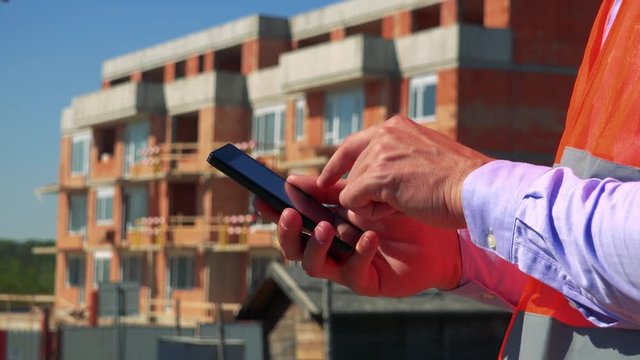 Construction worker works on the smartphone in front of building site - closeup