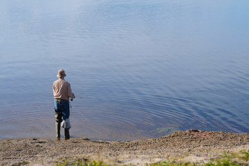 Fototapeta na wymiar A lone man fishing while standing on the ground at the water's edge