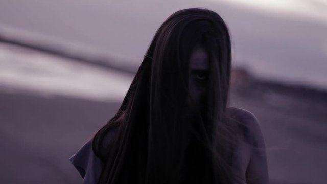 Beautiful female zombie walking on beach sad closeup purple color correction