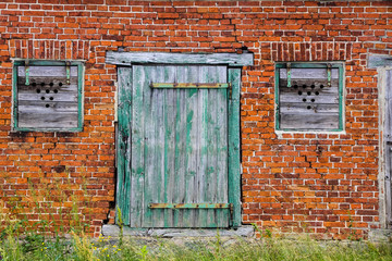 Old green wooden cracked door and windows with rusted metallic hinge on a retro red brick wall facade