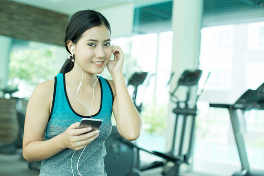 Asian Woman using Smartphone while Exercise at Gym. Woman do exercise alone with attractive Smiling. Woman with Exercise Concept