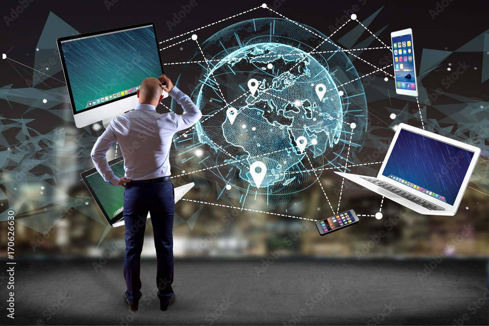 Poster Businessman in front of a wall with Computer and devices displayed on a futuristic interface with interantional network - Multimedia and technology concept