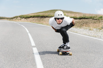 A guy wearing a helmet and sunglasses is riding his longboard on a country road