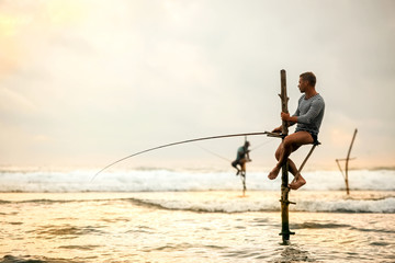 The European tourist is engaged in traditional fishing on poles in the Indian Ocean. Sri Lanka.