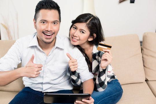Indonesian couple electronic shopping on tablet sitting on sofa