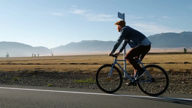 Young handsome man riding at vintage bicycle in the country road. Sporty guy cycling at the track. Male cyclist riding fixed gear bike at highway. Healthy active lifestyle 20s 4k.