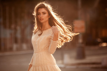 Beautiful young lady with long healthy hair and cute dress walking on the street. Hot summer...