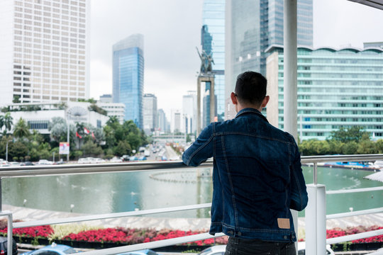 Rear view of a young man wearing blue denim jacket while looking at a historic monument in a famous district of Jakarta
