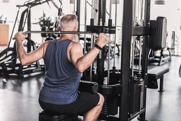 Concentrated senior male is doing exercises in modern gym