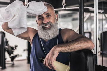 Positive old male is laughing while resting in gym