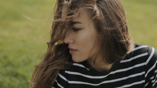 Happy woman sitting on grass, close up portrait of cute face in slowmotion