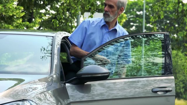 Senior man gets in the car on the street with trees 