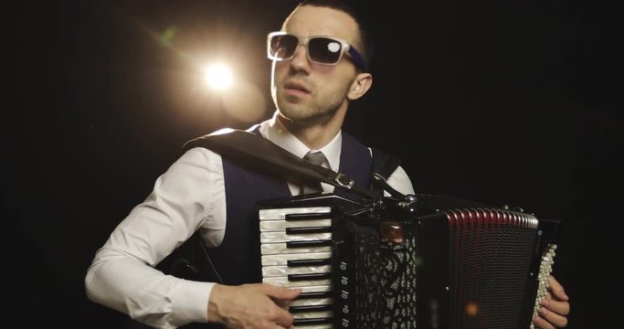 A fashionable musician in a white shirt plays the accordion in the studio on a black background.