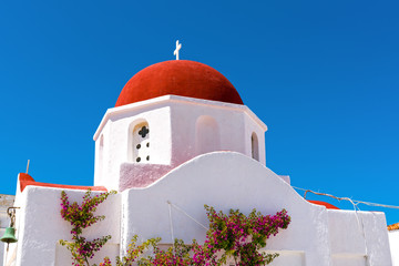 Traditional Greek church building with red dome and whitewashed facade under blue sky. Mykonos. Cyclades islands,  Greece. © vivoo