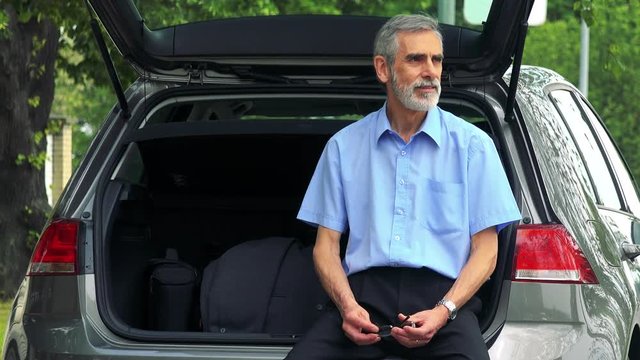 Senior man sits in the trunk and looks around - trees in the background