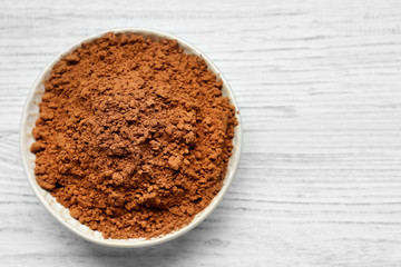 Plate with cocoa powder on white wooden background
