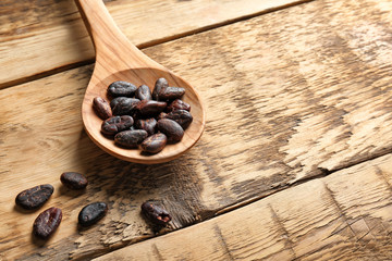 Spoon with aromatic cocoa beans on wooden table