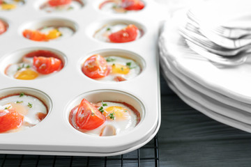 Muffin tin with tasty eggs, tomatoes and ham on table