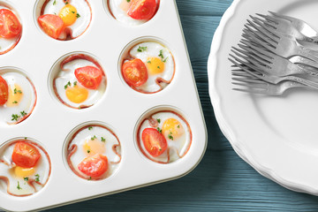 Muffin tin with tasty eggs, tomatoes and ham on table