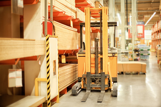 Forklift loader standing near shelves with wooden boards in storehouse