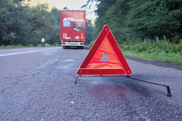 Red warning triangle on a road with a broken down truck.