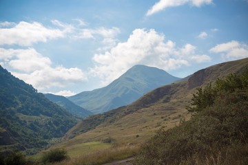 Горный пейзаж. Красивый вид на живописное ущелье, панорама горной местности, белые облака на синем небе. Природа и горы Северного Кавказа