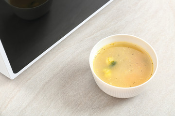 Bowl with soup near microwave on table