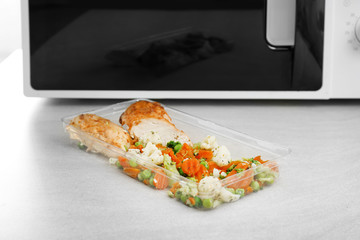 Plastic food container with delicious fried meat and baked vegetables on table