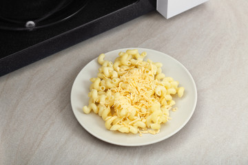 Plate with pasta and cheese near microwave on table