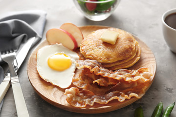 Tasty breakfast with fried egg, pancakes and bacon on wooden board