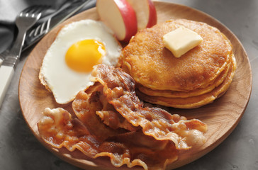 Tasty breakfast with fried egg, pancakes and bacon on wooden board