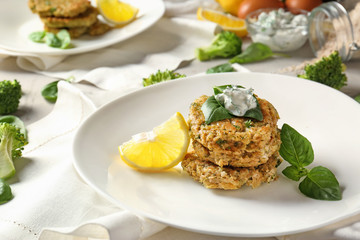 Broccoli pancakes served with sauce, lemon slice and basil leaves on white plate