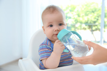 Mother giving baby bottle with water indoors