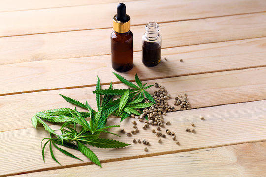 Hemp leaves and bottles of oil on wooden background
