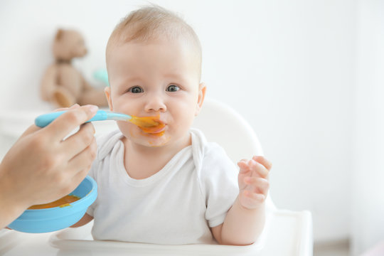 Mother feeding baby with spoon indoors